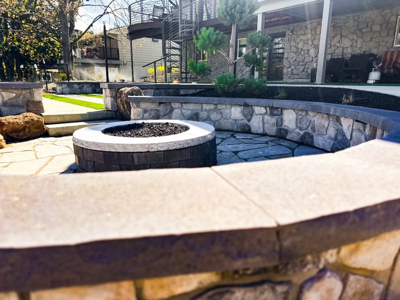 A curved stone seat wall around a fire pit on a terraced foothills backyard