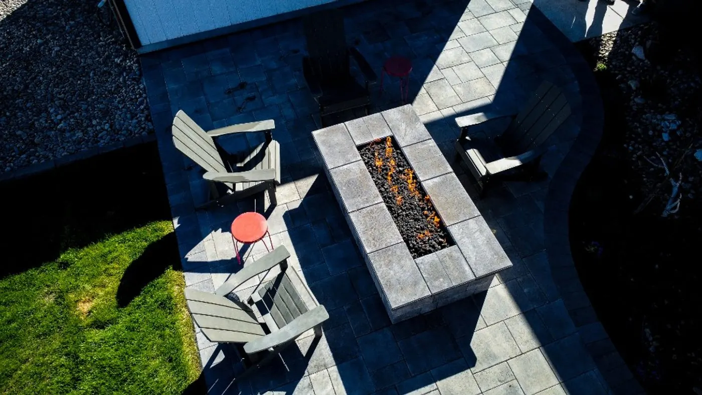 Overhead view of the fire table on the gray paver patio, with Adirondack chairs, two red side tables and the lawn alongside