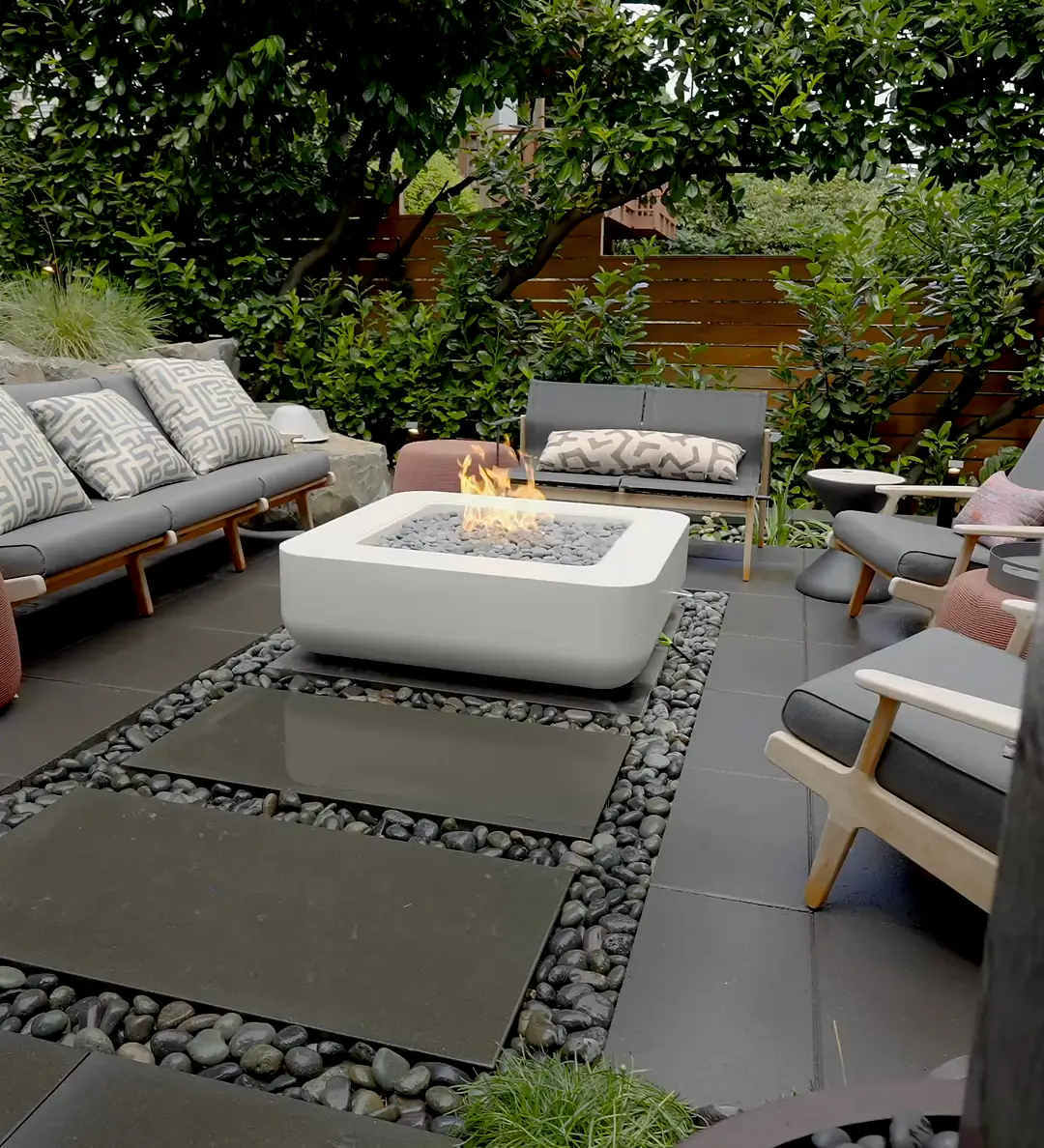 Outdoor lounge with sofas around a square fire table, on large slab pavers set in black river pebbles