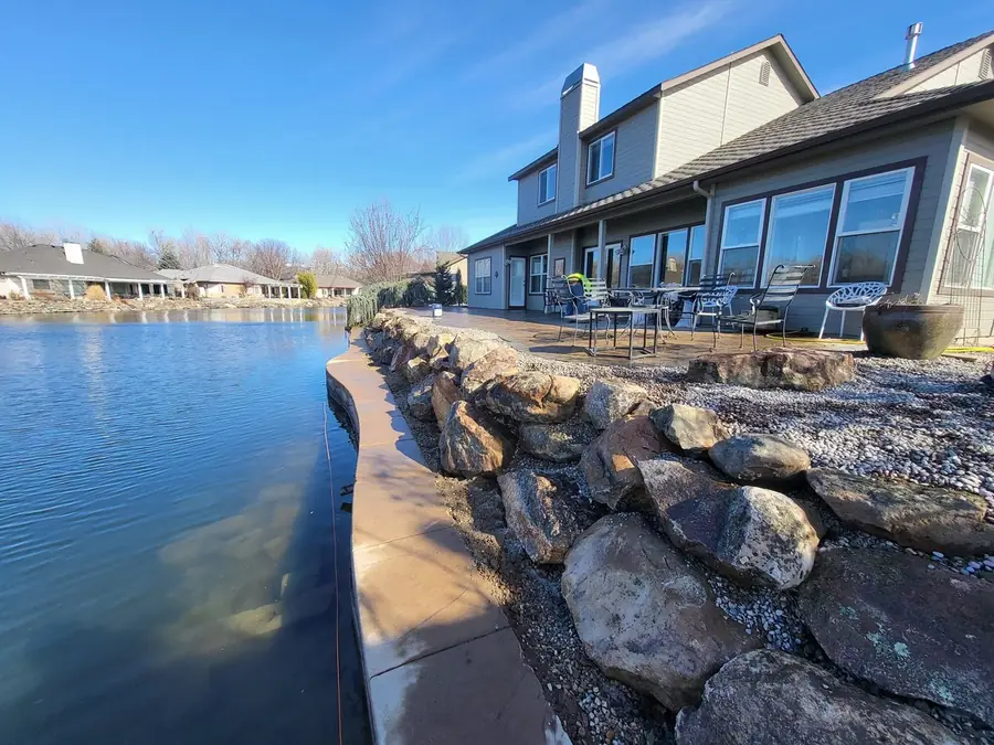 A boulder retaining wall along the water below a two-story home and its terrace